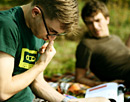 Link zur Seite „www.praktisch-unschlagbar.de“ (Junger Mann mit Hornbrille liest ein Buch und kratzt sich fragend an der Nase)