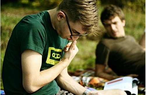 Junger Mann mit Hornbrille liest ein Buch und kratzt sich fragend an der Nase