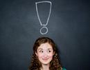 Link zur Seite „FAQs“ (Junge Frau vor Schultafel mit einem kreidegezeichneten Ausrufezeichen über dem Kopf)