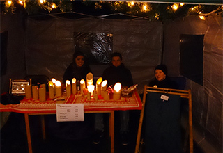 Drei Schüler der Schülerfirma "Bamboo Circle" beim Verkauf der Teelichthalter aus Bambus an einem Stand im Dunkeln