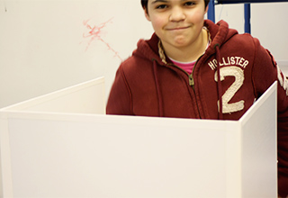 Ein Schüler der Schülerfirma "Leisebox" hinter einer weißen Box