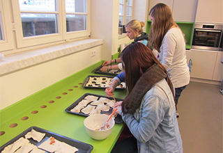 Die "Schülerfairma S-GmbH" beim Zubereiten von Teigtaschen auf einer grünen Arbeitsplatte
