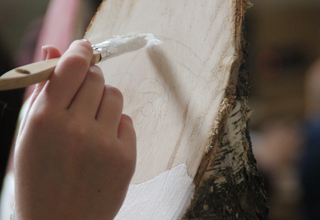Hand streicht mit einem Pinsel einen Holzscheit weiß