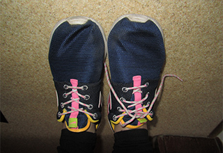 Dunkelblaue Turnschuhe mit pinken Schnürsenkeln. Der linke Schuh ist gebunden, der rechte ist offen.