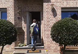 Schüler mit Rucksack geht durch eine Haustür