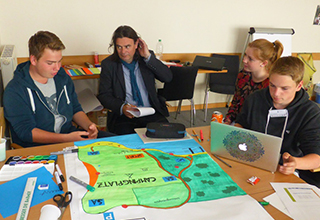 Teammitglieder von SurFüchse und ihr Betreuer sitzen am Tisch bei der Planungsarbeit