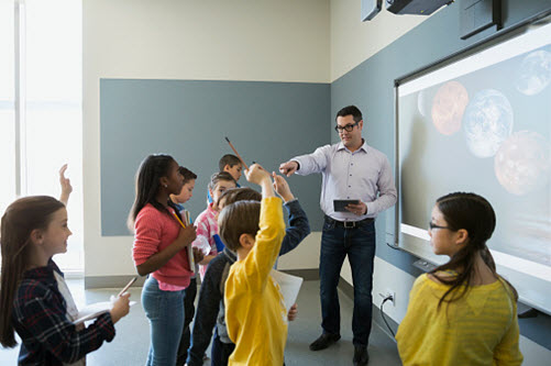 Lehrer steht mit seinem Schülern vor einer Sternenkarte, die an der Wand des Klassenraums hängt
