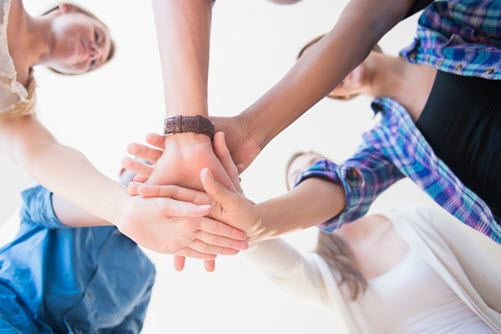 Schülerinnen und Schüler legen Hände übereinander als Zeichen von Teambuilding