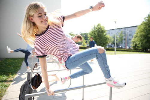 Junge blonde Frau in Jeans und Turnschuhen springt seitlich über ein Geländer