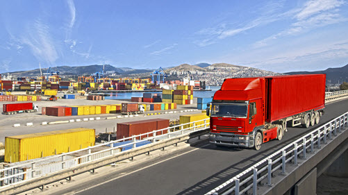 Roter Lastkraftwagen fährt an einem Container-Hafen vorbei