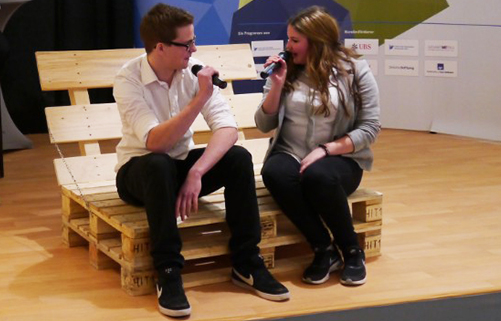 Interview: Zwei Schüler mit Mikrofonen sitzen auf Holzpaletten