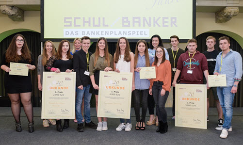 Gruppenbild aller Gewinnerteams von SCHUL/BANKER mit ihren Urkunden in der Hand, dahinter ein SCHUL/BANKER-Plakat mit der Aufschrift: SCHUL/BANKER Das Bankeplanspiel