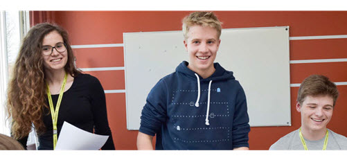 Eine Schülerin und zwei Schüler vor einem Whiteboard lachen