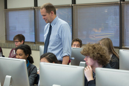 Lehrer mit seinen Schülern im Informatikraum, in dem die Schüler vor Computern sitzen