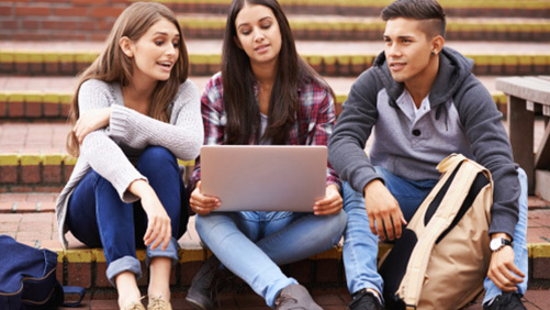 Zwei Schülerinnen und ein Schüler sitzen auf einer Treppe mit einem Laptop